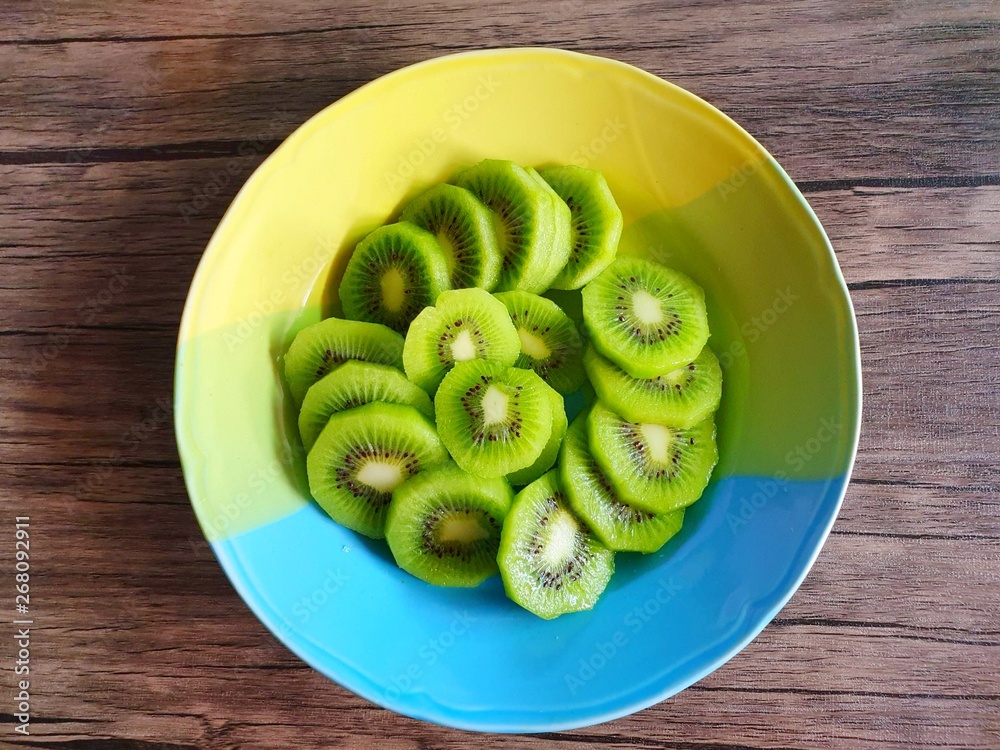 Top view of fresh sliced Kiwi fruit on colorful plate on wooden table, for making drinks or salads, healthy food concept Top view of fresh sliced Kiwi fruit on colorful plate on wooden table, for making drinks or salads, healthy food concept