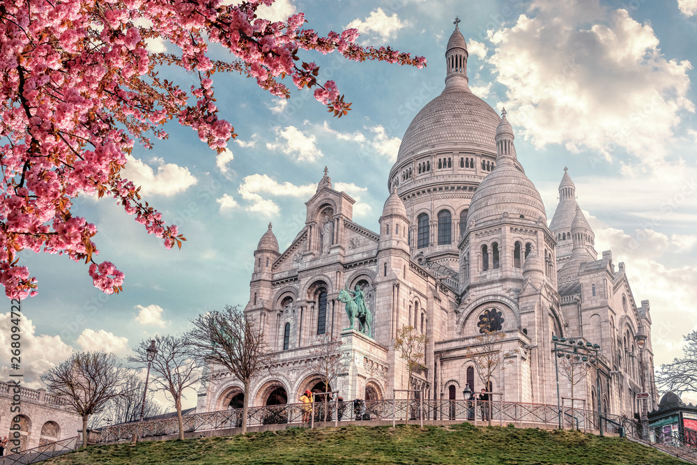 View of Basilica Sacre Coeur in Montmartre in Paris, France. Spring time with cherry blossom tree and blue sky.