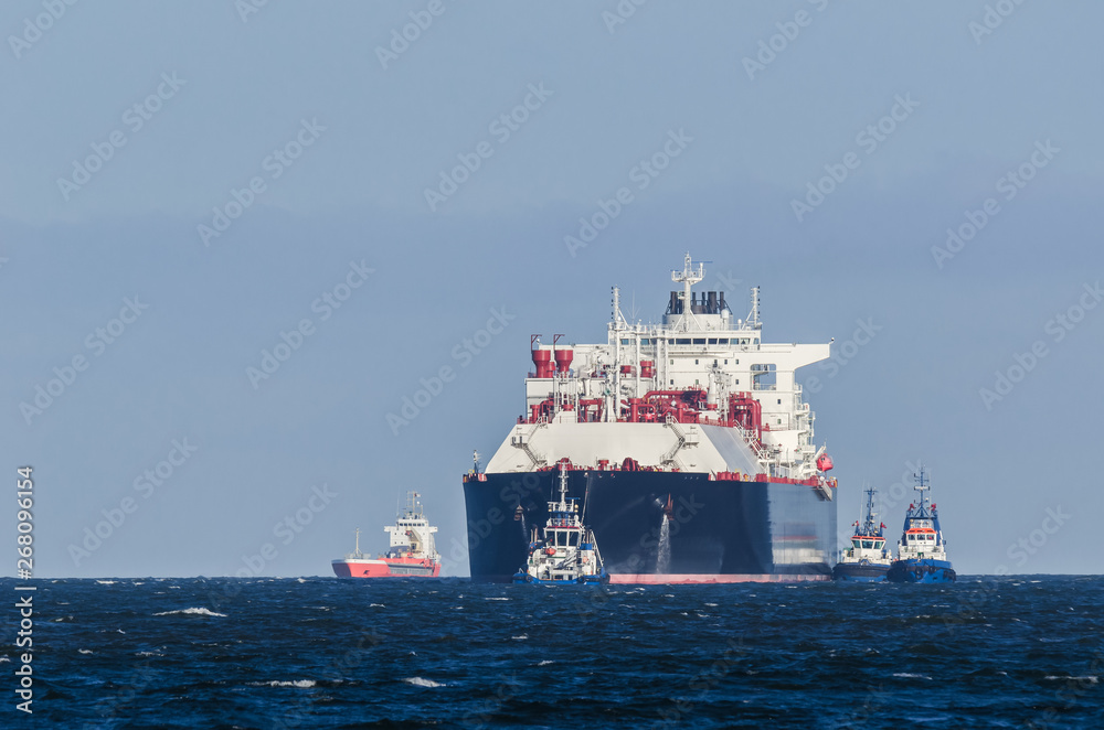LNG TANKER - A large ship belayed by tugboats travels by water to the port