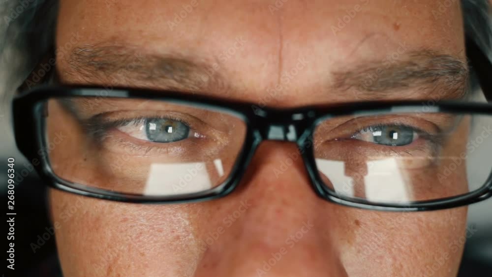 Close up of man with blue eyes working on computer and taking off eyeglasses to rub his eyes Close up of man with blue eyes working on computer and taking off eyeglasses to rub his eyes