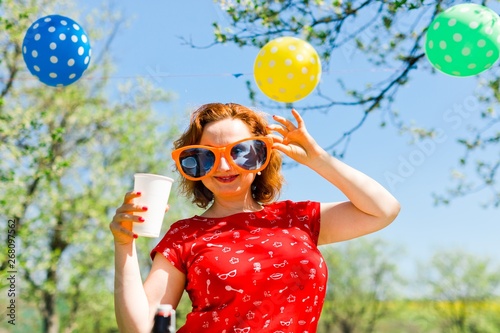 Woman posing in red dress and big funny sun glasses on garden party - summer picnic.