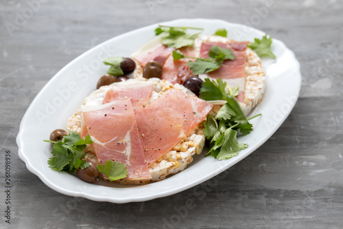 crispy rice diet toasts with prosciutto on ceramic background