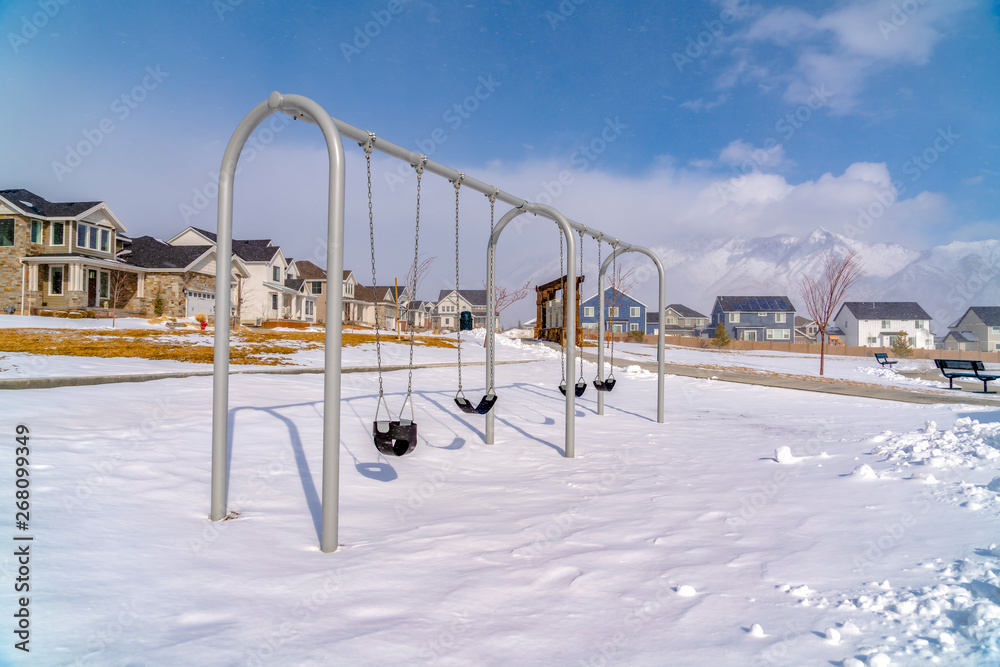 Baby swings at a playground blanketed with clean snow on a sunny winter day Baby swings at a playground blanketed with clean snow on a sunny winter day