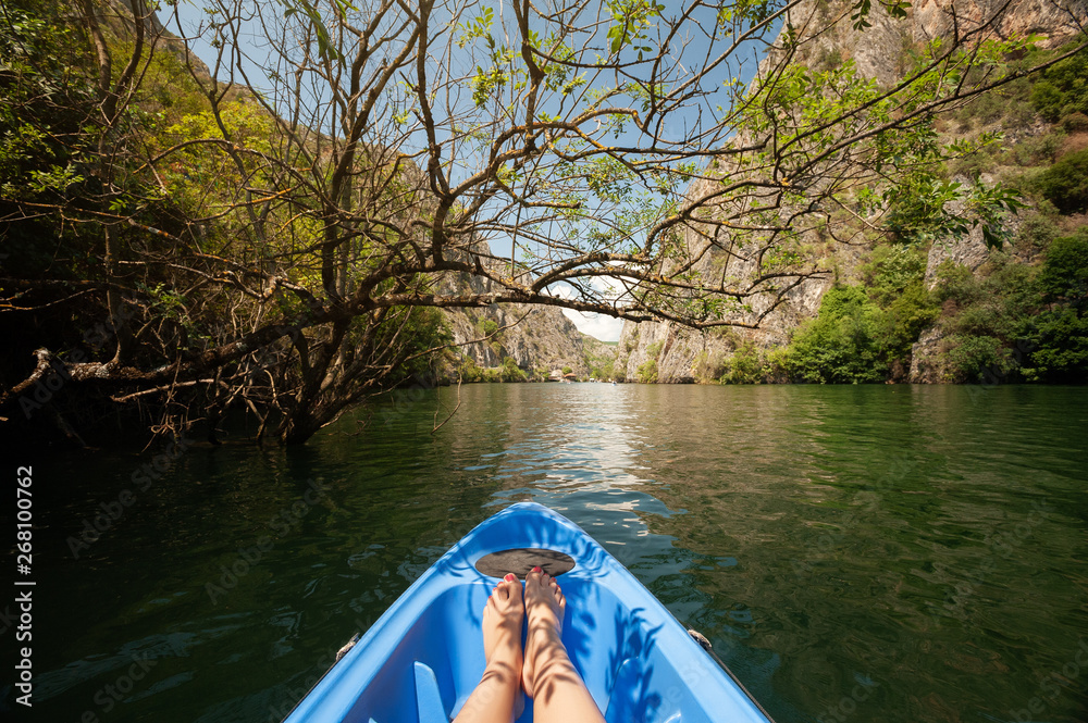 Fototapeta premium Kayaking through river in Matka canyon, Macedonia. Woman legs in the blue kayak