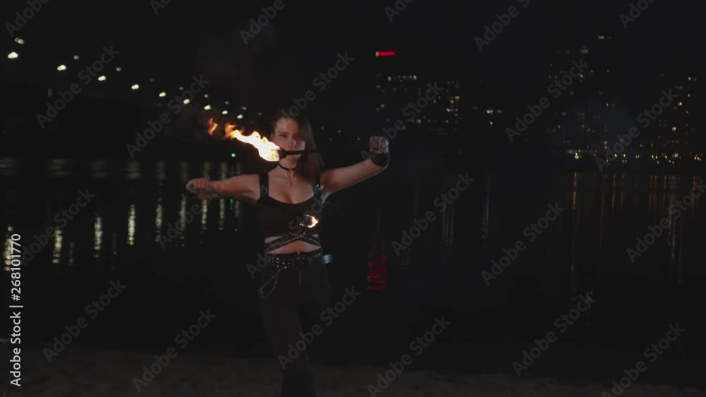 Attractive young female fireshow artist transfering to viewer energy and power of fire at night city. Redhead firegirl juggling burning torches outdoor performing magic show with flame. Attractive young female fireshow artist transfering to viewer energy and power of fire at night city. Redhead firegirl juggling burning torches outdoor performing magic show with flame.