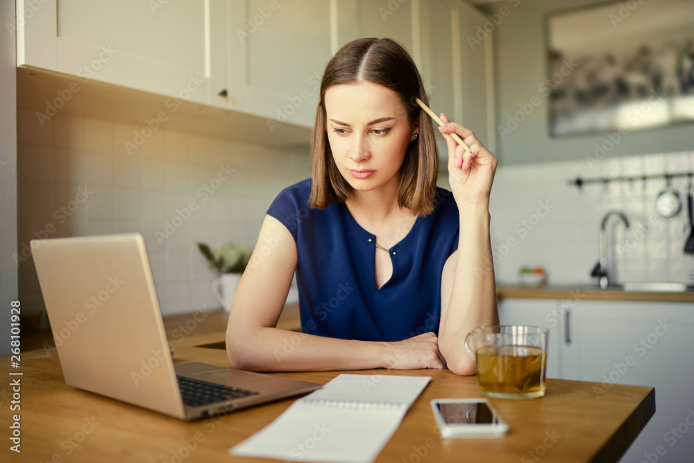 Working at home. Freelance concept. Thoughtful young woman using laptop in kitchen. Working at home. Freelance concept. Thoughtful young woman using laptop in kitchen.
