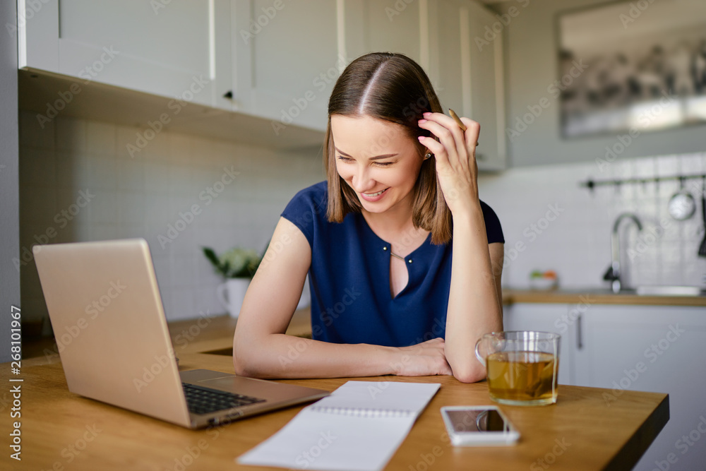 Ideas for business. Studying and working at home. Freelance concept. Thoughtful young woman making notes using laptop in kitchen. Ideas for business. Studying and working at home. Freelance concept. Thoughtful young woman making notes using laptop in kitchen.