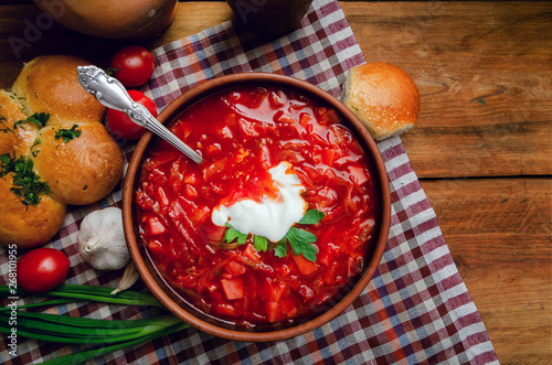 Ukrainian national cuisine - red borsch with donuts in a clay bowl on a wooden table.
