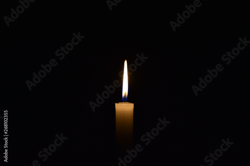 Candle burning in the black background. Located on the center of the shot.