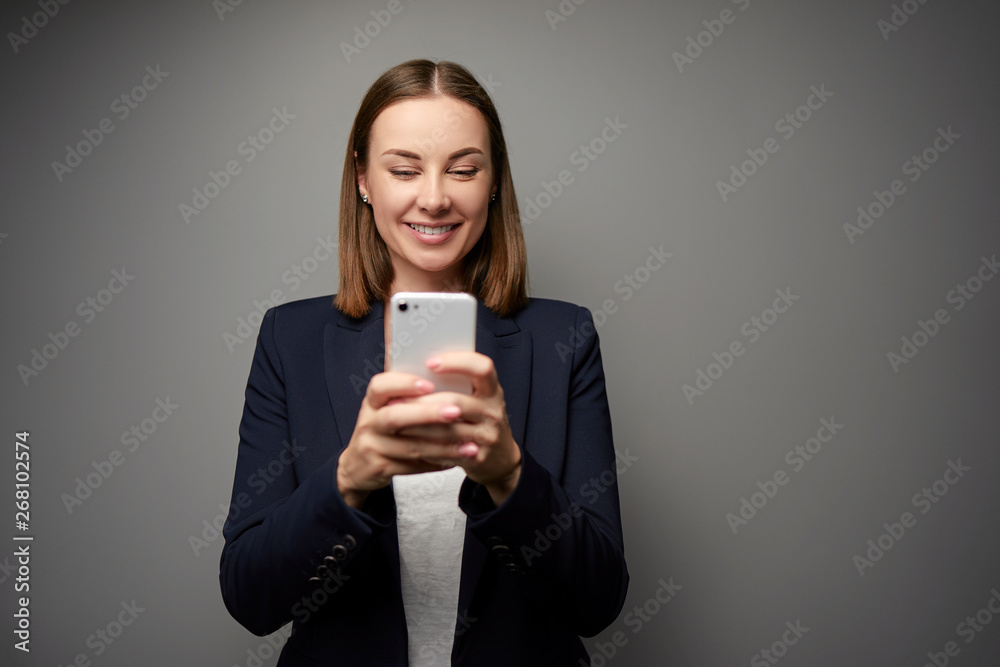 Business and technology. Confident young woman in formal wear using smart phone against grey wall. Business and technology. Confident young woman in formal wear using smart phone against grey wall.