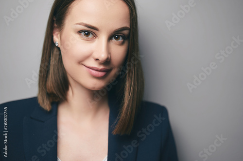 Close up studio portrait of oung businesswoman in suit looking at camera. Grey background.