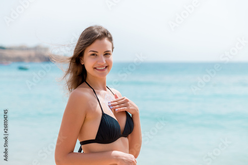 Young attractive woman is protecting her skin on the breast with sunblock at the sunny beach