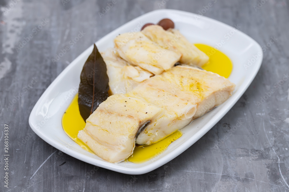 boiled cod fish with olive oil on white dish on ceramic background