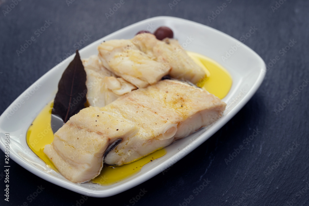 boiled cod fish with bay leaf and olive oil on white dish on ceramic background