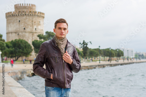 Handsome man, tourist, stands near a White Tower in the center Thessaloniki, Greece in front of a sea