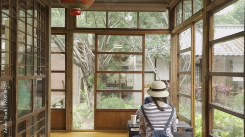 beautiful japanese style wooden house with green spring teien garden. back view two asian woman friends sitting in corner doing chado ceremony chatting sitting on floor. girls talking relaxing enjoy photo