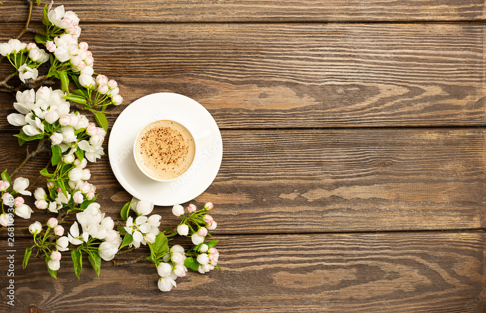A cup of hot aromatic coffee and a blossoming branch of an apple tree on a wooden background. Flat layout. View from above. Copy space. A cup of hot aromatic coffee and a blossoming branch of an apple tree on a wooden background. Flat layout. View from above. Copy space.