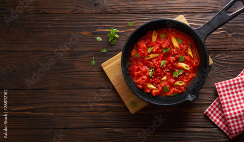 Pasta penne with tomato sauce and basil on iron cast pan. Wooden table, top view with copy space