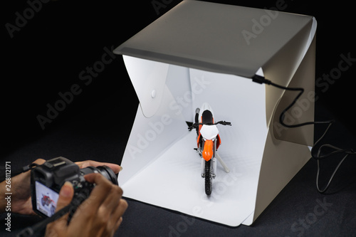 Amateur photographer working on mirrorless camera to shooting motrocycle model in mini lightbox