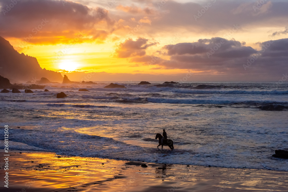 Horseriding at ocean beach on sunset background. Canary island.