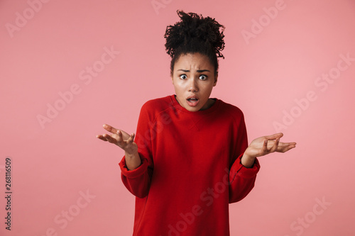 Beautiful young confused african woman posing isolated over pink wall background.