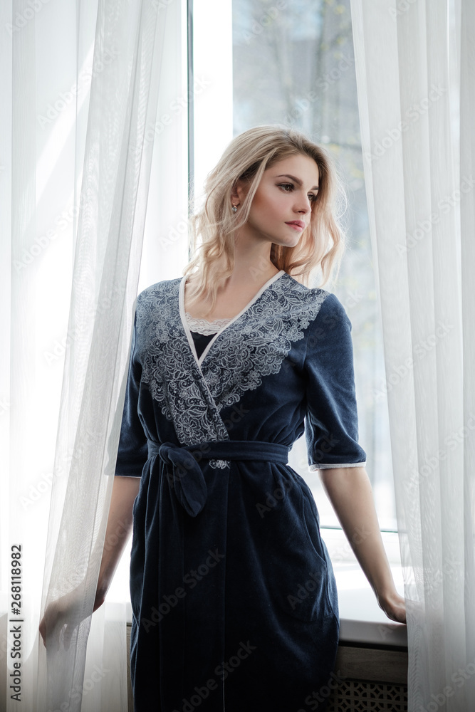 Beautiful young woman blonde in a blue robe by the window. Beautiful young woman blonde in a blue robe by the window.