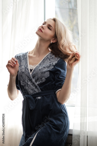 Beautiful young woman blonde in a blue robe by the window.