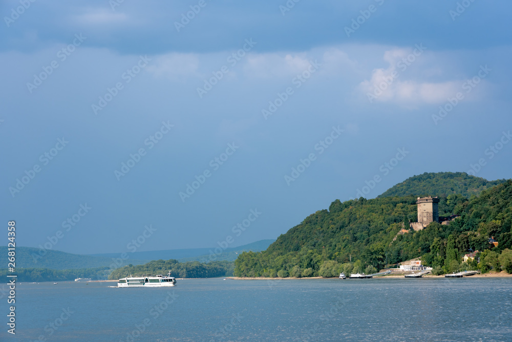 Cruise ship on Danube river. Wooded shore, old castle tower