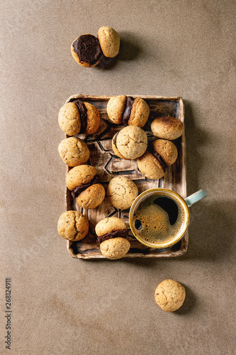 Baci di dama homemade italian hazelnut biscuits cookies with chocolate cream served in ceramic tray with cup of espresso coffee over brown texture background. Flat lay, space