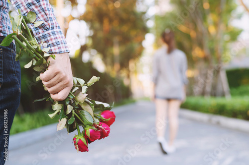 Billede på lærred young man standing with a Red Rose on Hand Sadness Love in Ending Break up of Relationship Blurred woman Back Side Walking away parting  in public park outdoor