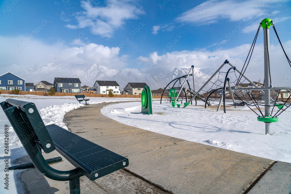 An empty bench facing a playground with snow covered ground in winter An empty bench facing a playground with snow covered ground in winter