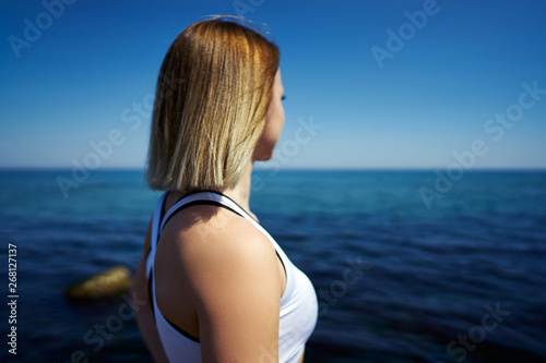 Back view of a beautiful girl who looks into the sea or ocean on a sunny day.