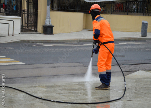 Worker washes the pavement with water from a hose