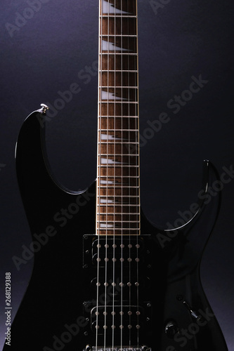 Body and neck of electric guitar. Close up detail. Accentuated shapes by illumination. With copy space on dark backgrouna