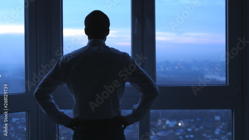 Back view of businessman stand near the window and looks on night city background