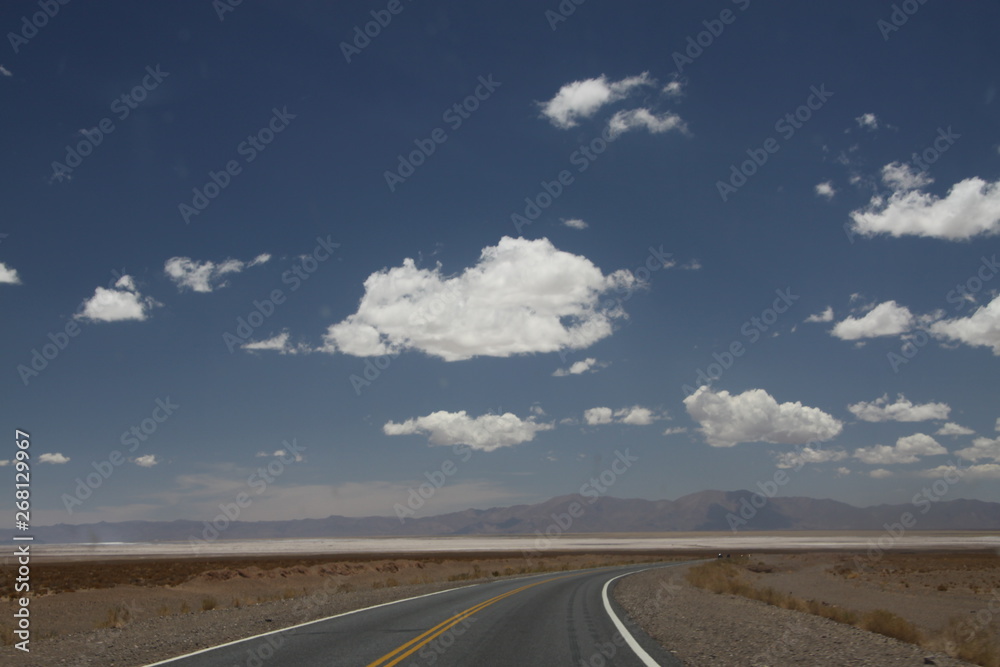asfaltowa droga prowadząca do wielkiej solnej równiny w argentynie z andami i niebem w tle - obrazy, fototapety, plakaty 
