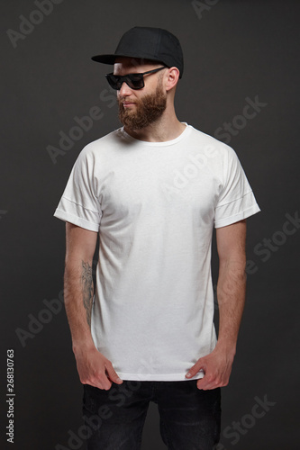 Hipster handsome male model with beard wearing white blank t-shirt and a baseball cap with space for your logo or design in casual urban style