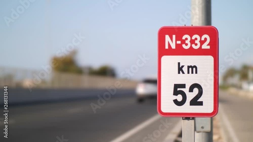 Many vehicles drive past a kilometer sign on the four-lane national road N332 in Spain in the sunshine and beautiful soft bokeh in the background.