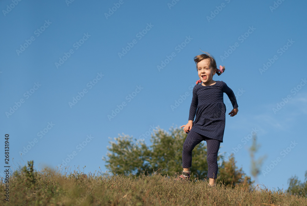 Little four years old girl in blue dotted dress playing outdoor. Happy kidding child with tongue out under blue sky. Concept - happy lifestyle.