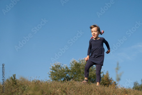 Little four years old girl in blue dotted dress playing outdoor. Happy kidding child with tongue out under blue sky. Concept - happy lifestyle.