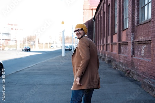 Portrait of stylish handsome young man in glasses with bristle standing outdoors. Man wearing jacket and shirt.