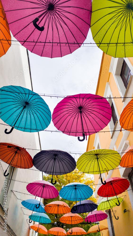 Obraz premium Beautiful colorful umbrellas hanging between building at old tow. Modern art installation on street