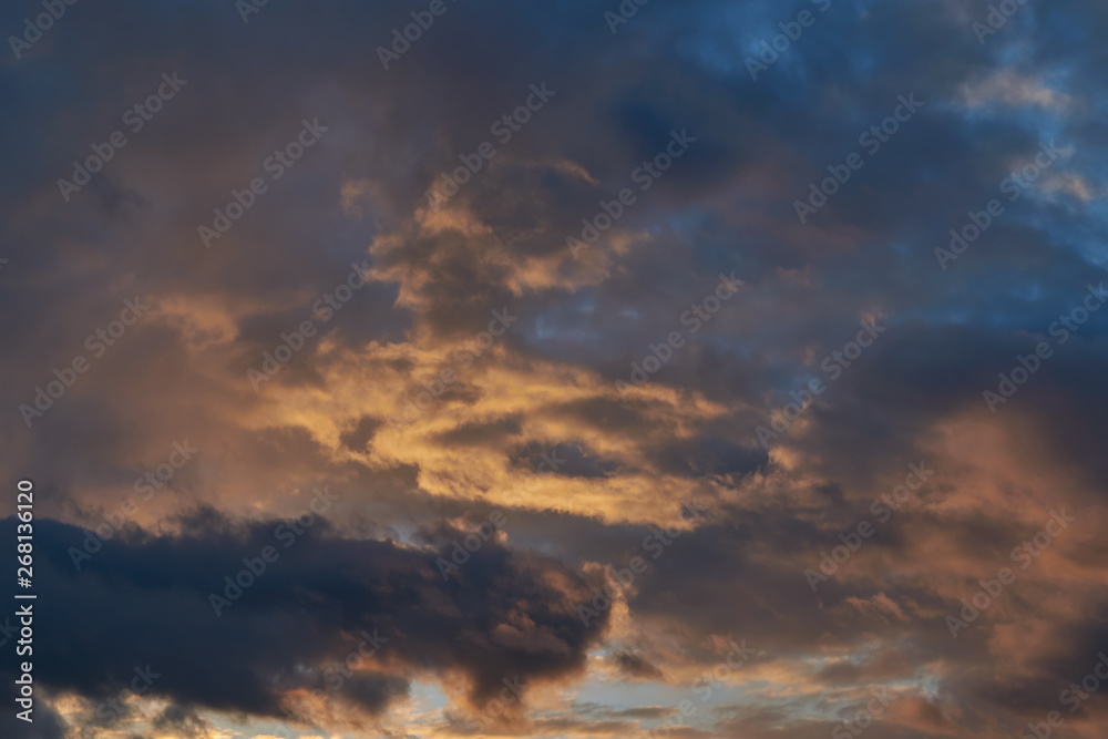 Dark blue and bright red Cumulus rain clouds illuminated by the evening sun. Clouds are coming and foretell rain and bad weather. Weather forecast, meteorology. Nature and atmosphere.