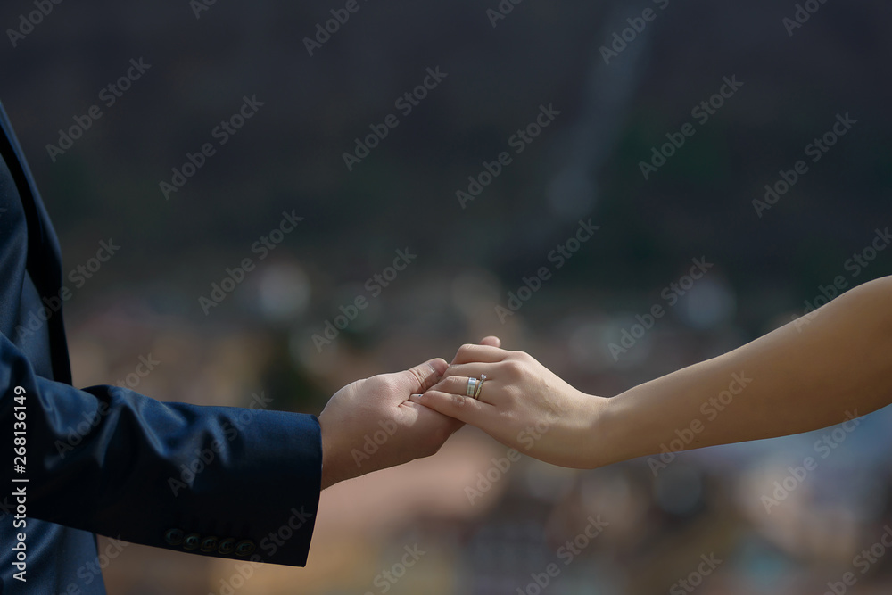Heterosexual Caucasian couple holding hands with visible engagement and wedding rings, with a blurred, out-of-focus background, concept for a couple in love, marriage, togetherness and commitment