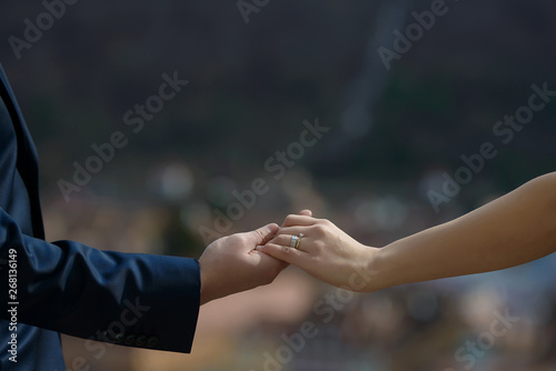 Heterosexual Caucasian couple holding hands with visible engagement and wedding rings, with a blurred, out-of-focus background, concept for a couple in love, marriage, togetherness and commitment © Ana