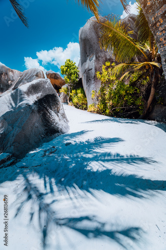 Walking pathway along the beach between giant granite boulders on Anse Source D Argent, La Digue island Seychelles. Contrast shadow of palm leaves on the ground. Vacation travel concept photo