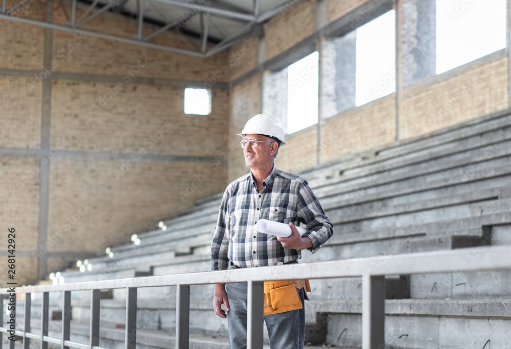 Portrait of senior construction worker with blueprint controlling building site.