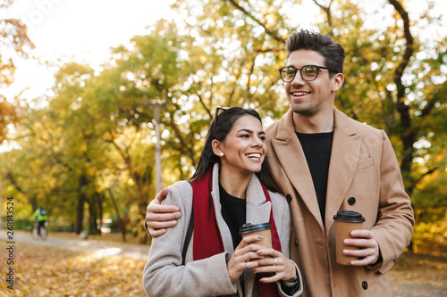 Portrait of caucasian couple drinking takeaway coffee from paper cups while walking in autumn park