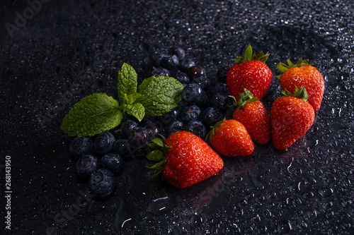 fresh red strawberries and blueberries macro on black table waterdrops