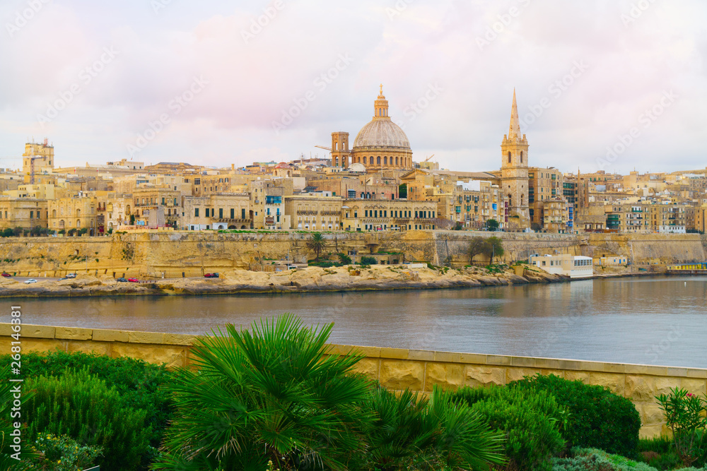Valletta morning skyline with Basilica of Our Lady of Mount Carmel as seen from Sliema, Malta. Green plants landscape design garden foreground. Horizontal summer background or wallpaper.
